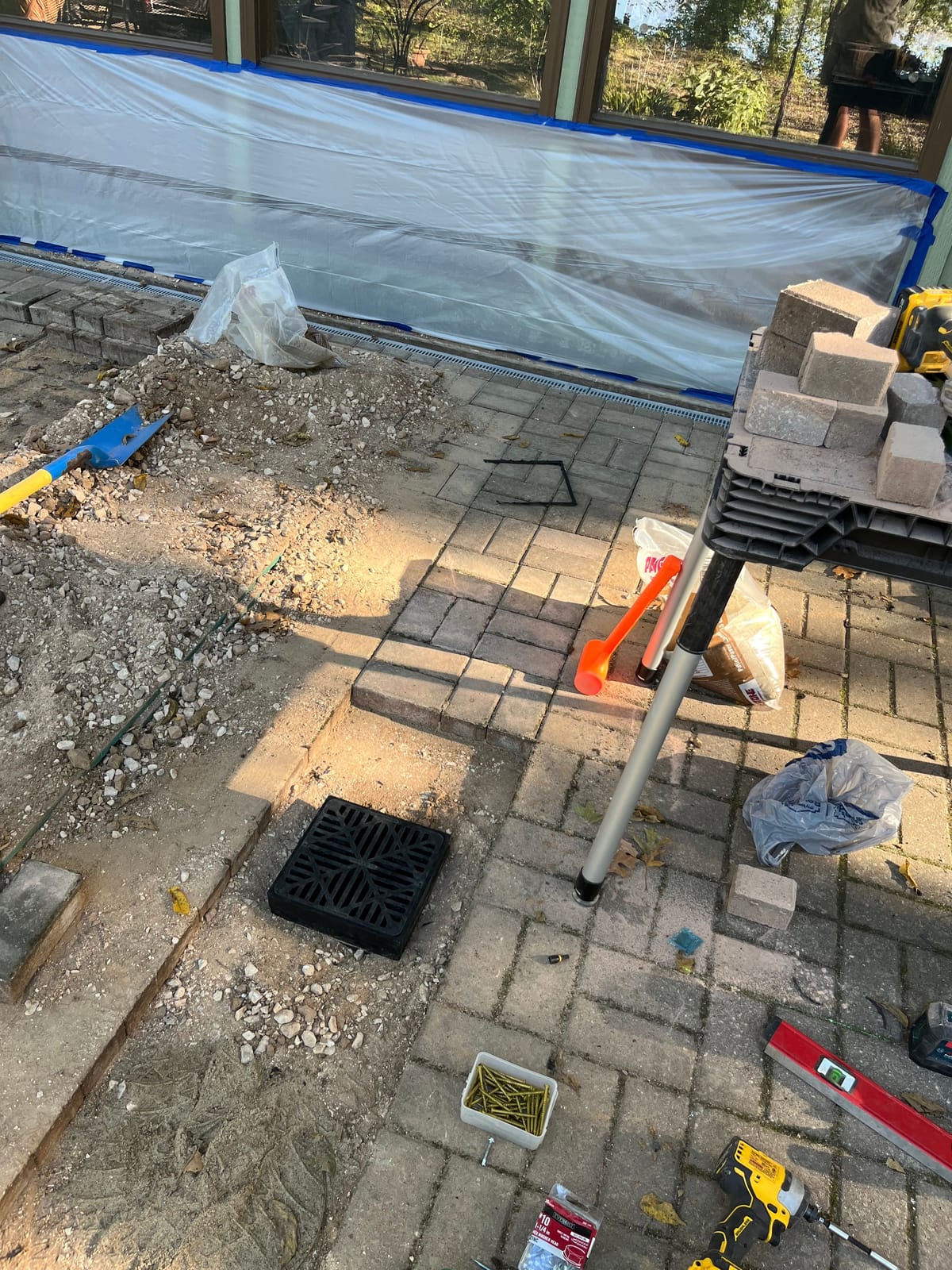 Black catch basin grate set into the compacted base of a patio before pavers are relaid around it