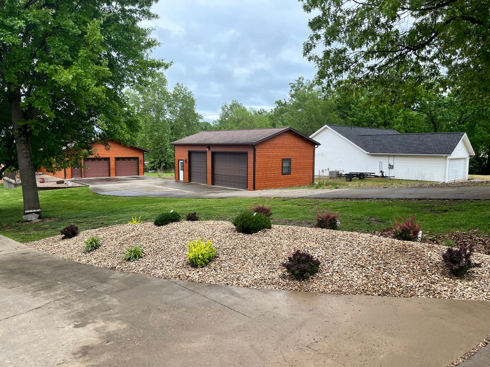 Wide gravel planting bed curving along a concrete driveway with new shrubs in front of a detached garage