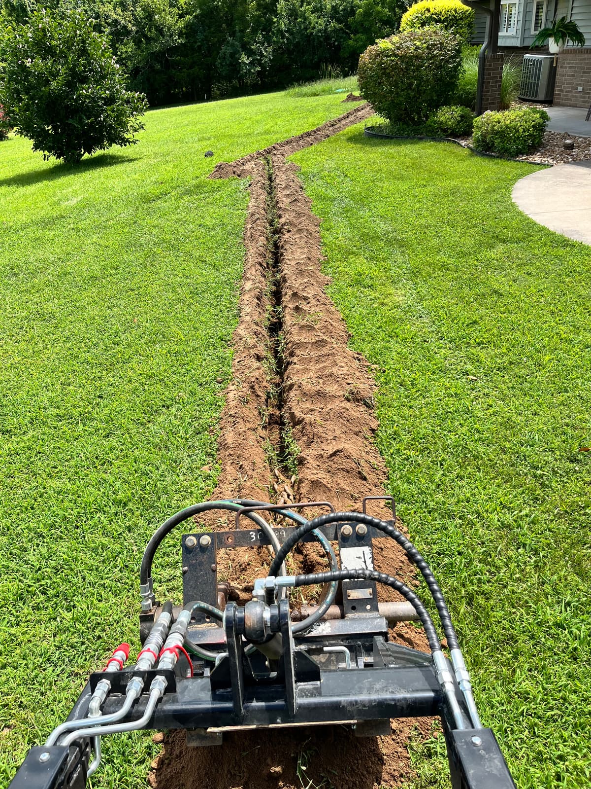 Trenching machine cutting a narrow line across a healthy green lawn to pull new irrigation pipe