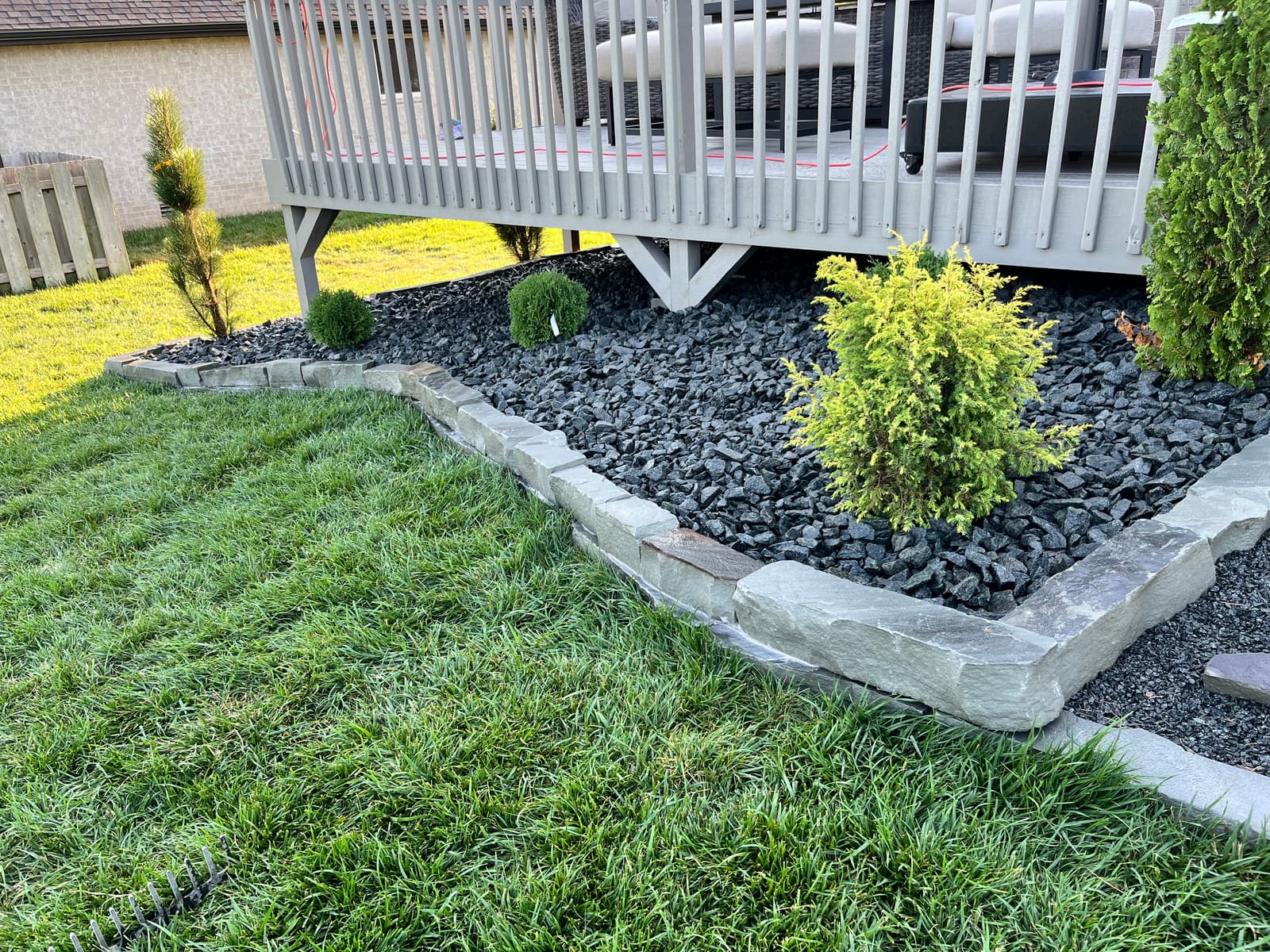 Cut stone edging holding a black rock bed with a gold-tipped shrub, meeting a crisp lawn line